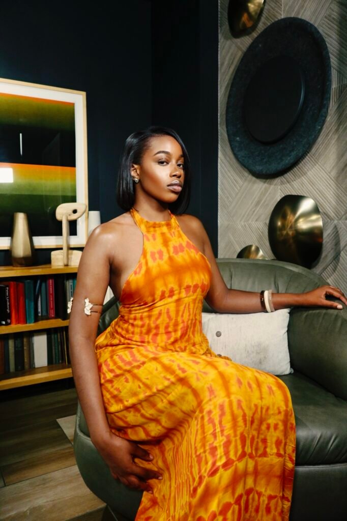 Model seated in the Belle de Dos halter dress in Sunset Orange tie-dye